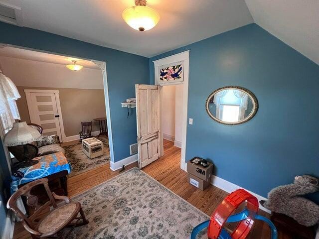 bedroom featuring visible vents, baseboards, lofted ceiling, and wood finished floors