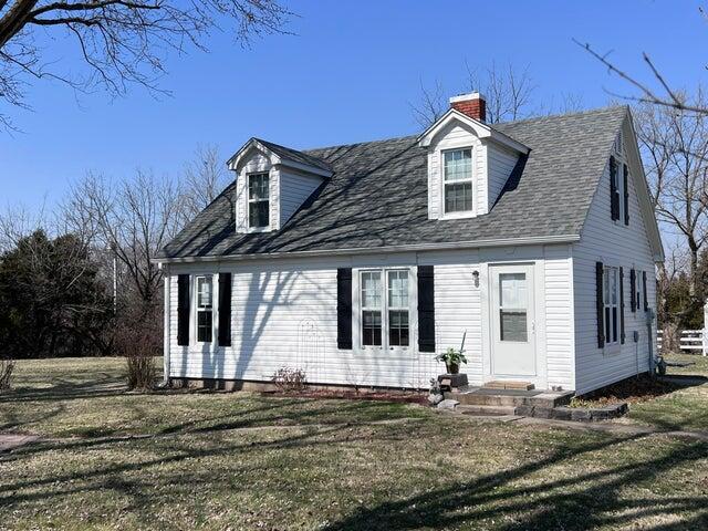 cape cod-style house with entry steps, a front yard, a shingled roof, and a chimney