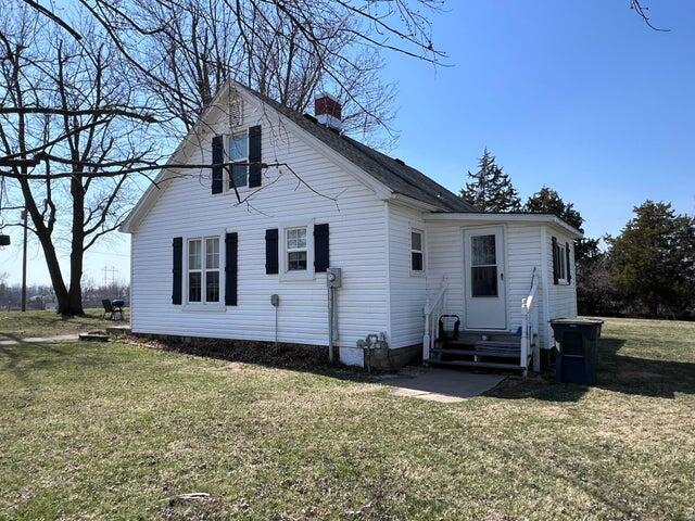 back of property featuring entry steps, a lawn, and a chimney