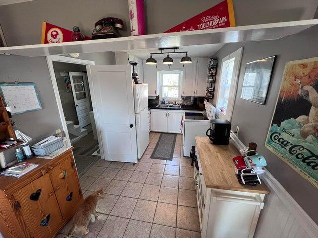 kitchen with light tile patterned floors, freestanding refrigerator, stove, white cabinetry, and a sink