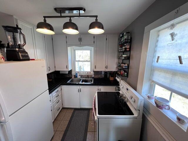 kitchen with dark countertops, freestanding refrigerator, electric range, white cabinetry, and a sink