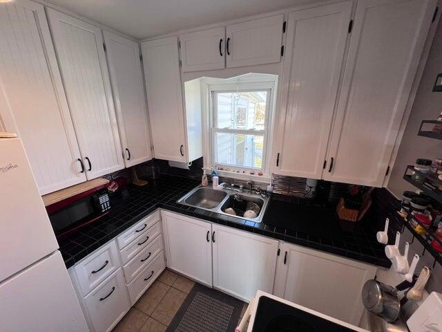 kitchen with tile patterned flooring, white cabinets, tile counters, and a sink