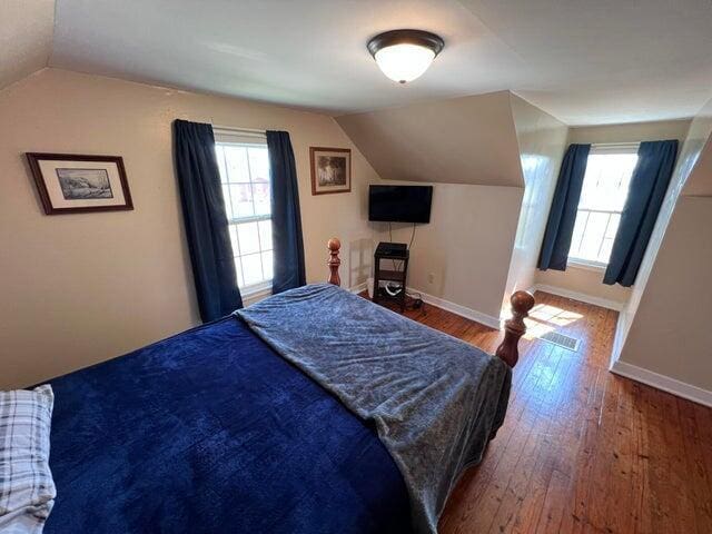 bedroom with hardwood / wood-style floors, vaulted ceiling, visible vents, and baseboards