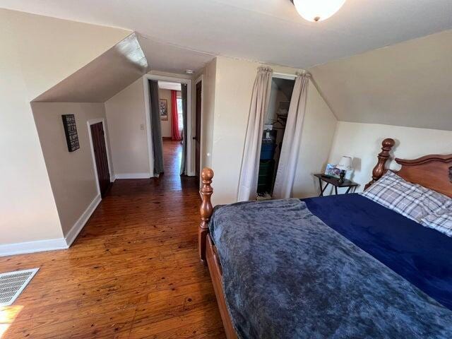 bedroom featuring visible vents, baseboards, wood finished floors, and vaulted ceiling