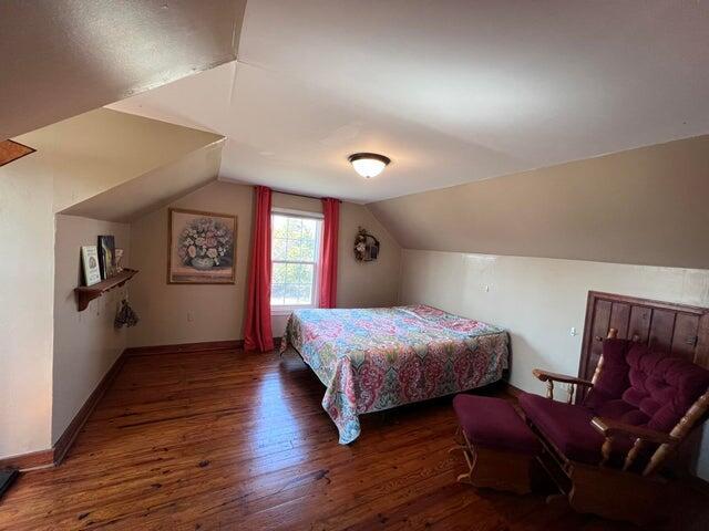 bedroom with vaulted ceiling, wood finished floors, and baseboards