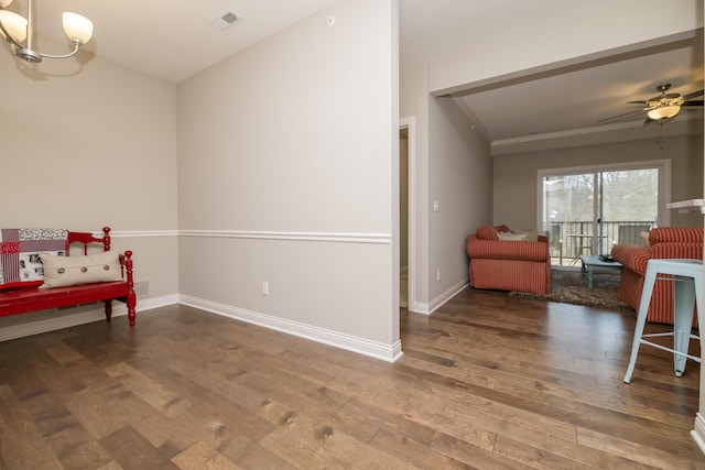 sitting room with wood finished floors, visible vents, baseboards, ornamental molding, and ceiling fan with notable chandelier