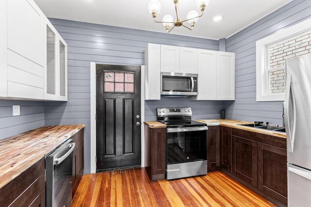 kitchen featuring light wood finished floors, stainless steel appliances, white cabinets, a chandelier, and butcher block counters