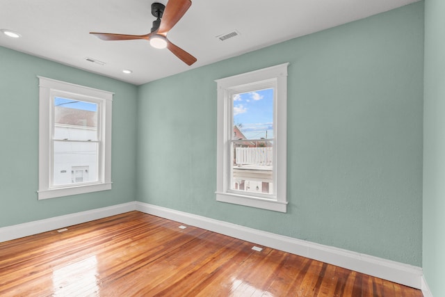 empty room featuring a ceiling fan, wood finished floors, visible vents, and a wealth of natural light