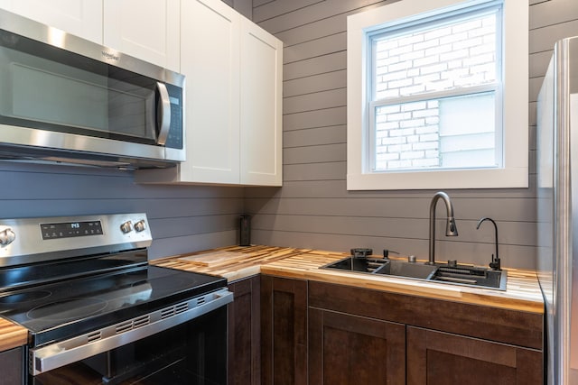 kitchen with white cabinetry, butcher block counters, stainless steel appliances, and a sink