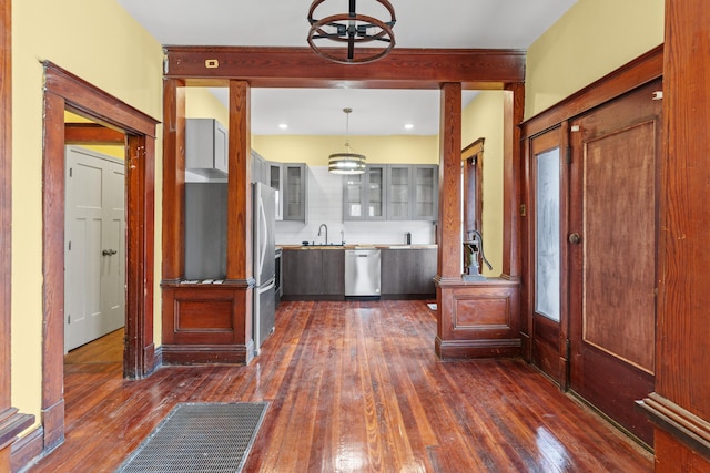 interior space with a sink, glass insert cabinets, appliances with stainless steel finishes, a notable chandelier, and dark wood-style flooring