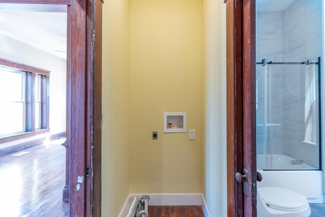 full bath with enclosed tub / shower combo, toilet, baseboards, and wood finished floors