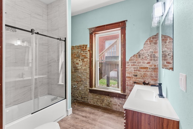 bathroom featuring vanity, wood finished floors, combined bath / shower with glass door, and brick wall