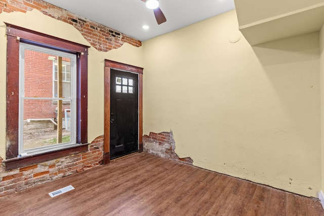 foyer entrance with visible vents, brick wall, wood finished floors, and a ceiling fan