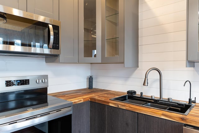 kitchen with gray cabinets, a sink, stainless steel appliances, glass insert cabinets, and wood counters