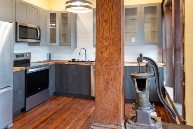 kitchen with a sink, dark wood-style floors, stainless steel appliances, glass insert cabinets, and wooden counters