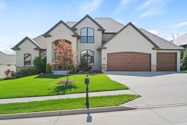 french country home featuring stucco siding, stone siding, a front yard, concrete driveway, and an attached garage