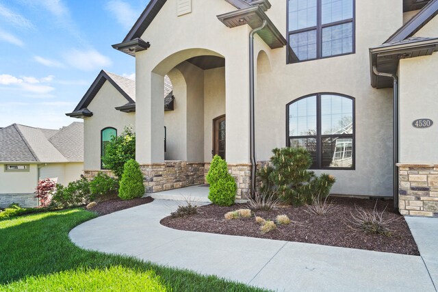 entrance to property featuring a lawn, stone siding, and stucco siding