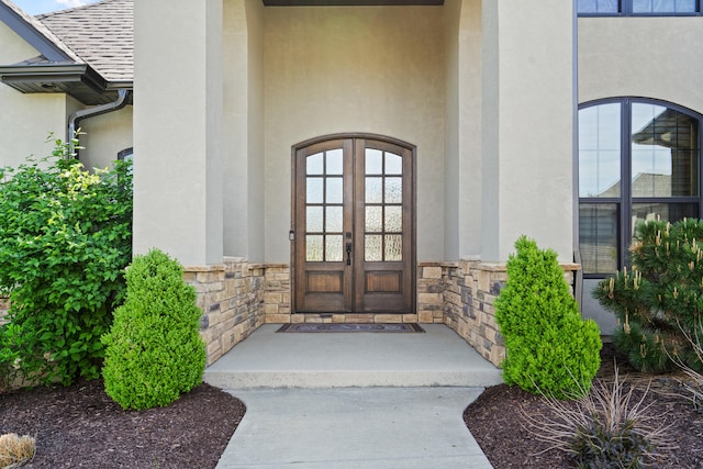 view of exterior entry featuring stucco siding, roof with shingles, french doors, and stone siding