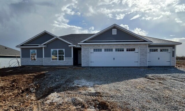 view of front facade featuring stone siding, an attached garage, and gravel driveway