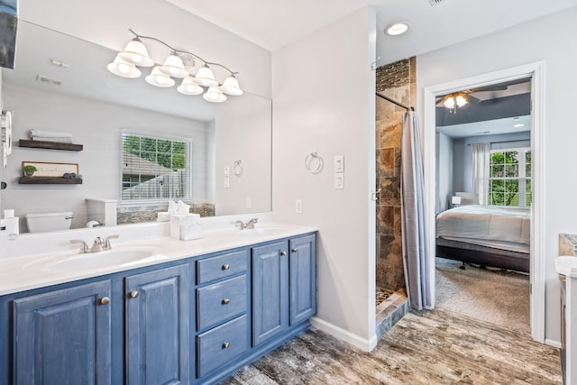 ensuite bathroom featuring double vanity, a sink, wood finished floors, and a tile shower