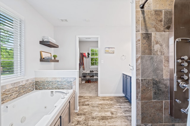 full bath featuring a jetted tub, a wealth of natural light, tiled shower, and wood finished floors