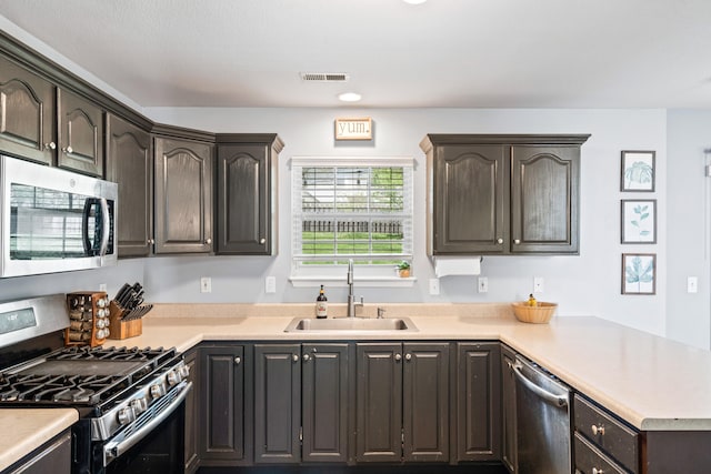 kitchen with visible vents, a peninsula, light countertops, a sink, and appliances with stainless steel finishes