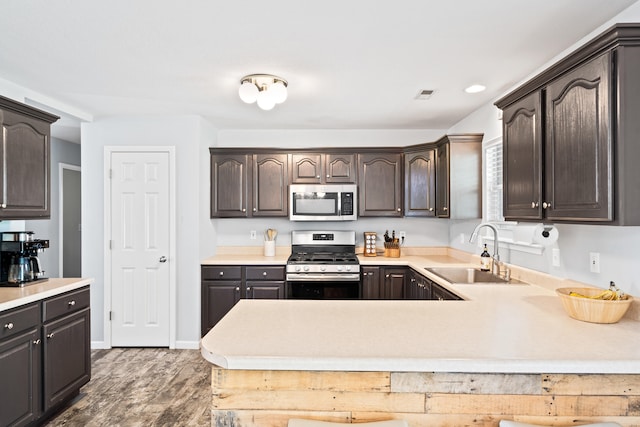 kitchen with dark brown cabinets, appliances with stainless steel finishes, a sink, light countertops, and wood finished floors