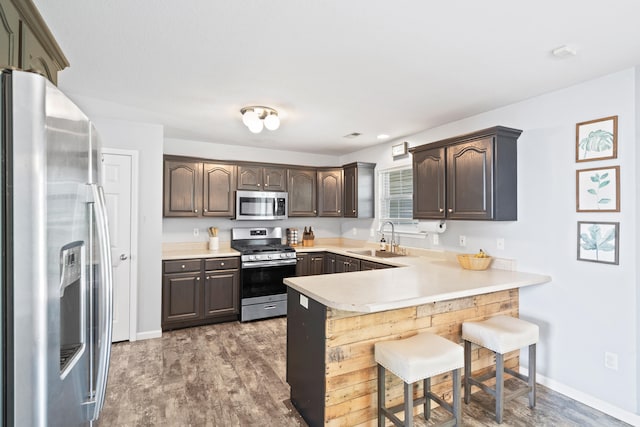 kitchen featuring dark brown cabinetry, a sink, light countertops, stainless steel appliances, and a peninsula
