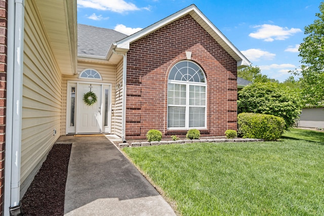 property entrance featuring a yard, brick siding, and a shingled roof