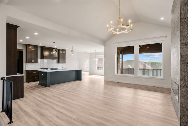 kitchen with an inviting chandelier, lofted ceiling, premium range hood, and a center island with sink