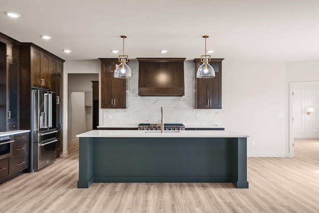 kitchen featuring dark brown cabinetry, light countertops, custom range hood, light wood-style flooring, and appliances with stainless steel finishes