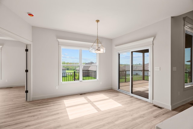 unfurnished dining area with baseboards, visible vents, light wood-type flooring, and a chandelier