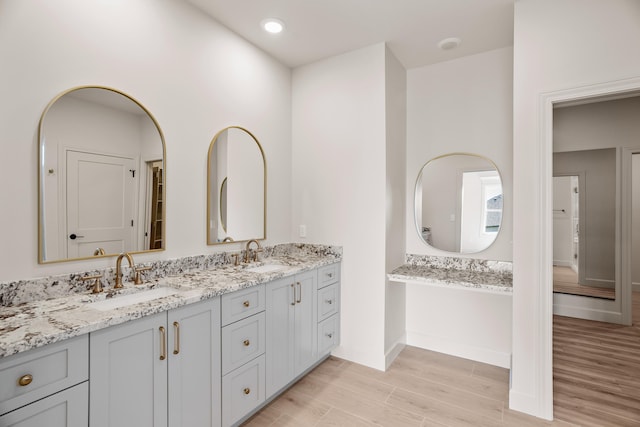 full bathroom featuring a sink, baseboards, double vanity, and wood finished floors