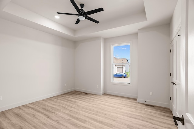 unfurnished room with light wood-style floors, a raised ceiling, ceiling fan, and baseboards