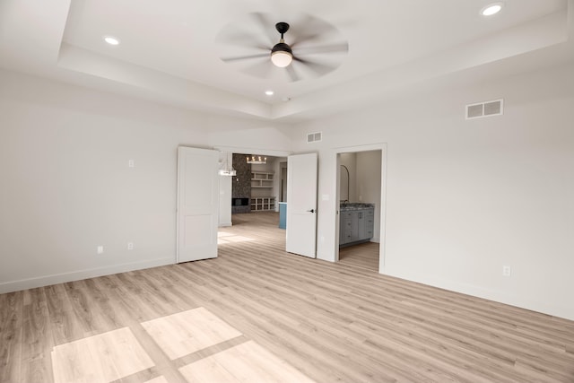 unfurnished bedroom with a tray ceiling, light wood-style flooring, and visible vents