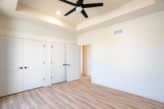 unfurnished bedroom featuring visible vents, baseboards, light wood finished floors, and a tray ceiling