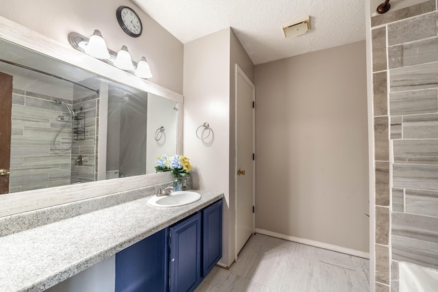 bathroom featuring baseboards, tiled shower, vanity, and a textured ceiling