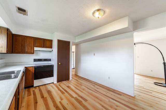 kitchen featuring light countertops, visible vents, light wood finished floors, a sink, and electric range
