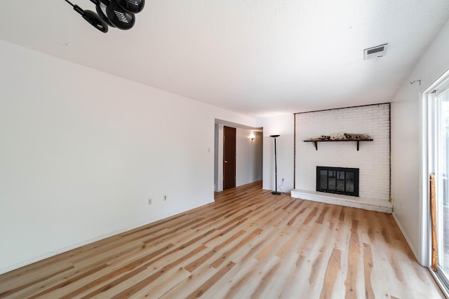 unfurnished living room with a brick fireplace, light wood finished floors, and visible vents