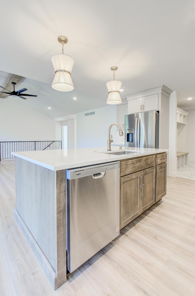 kitchen featuring stainless steel appliances, light countertops, visible vents, a sink, and a center island with sink