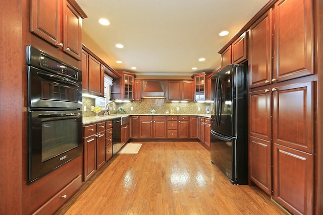 1204 S Walnut Ave, Salisbury, MO 65281 - kitchen with light wood-style floors, glass insert cabinets, tasteful backsplash, black appliances, and premium range hood