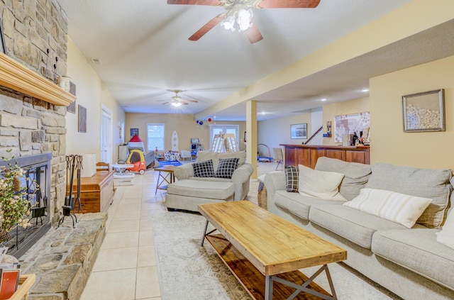 living area with light tile patterned floors, a stone fireplace, and ceiling fan