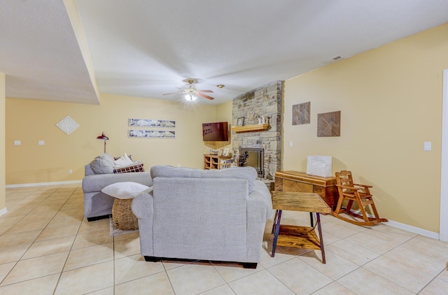 living area featuring light tile patterned flooring, a stone fireplace, a ceiling fan, and visible vents