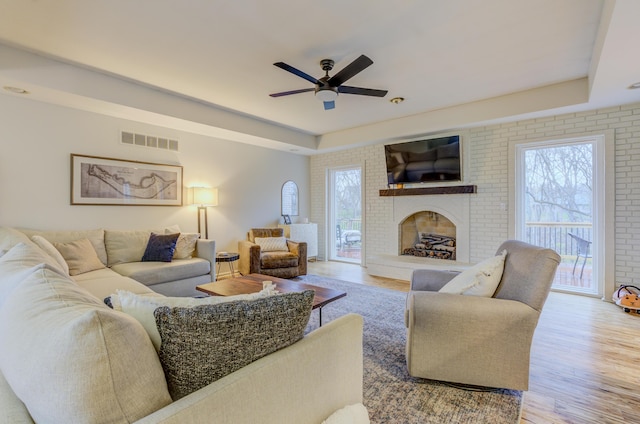 living room with visible vents, a raised ceiling, brick wall, ceiling fan, and wood finished floors