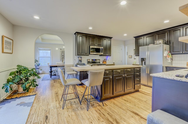 kitchen featuring light wood-style floors, tasteful backsplash, arched walkways, a kitchen island, and appliances with stainless steel finishes