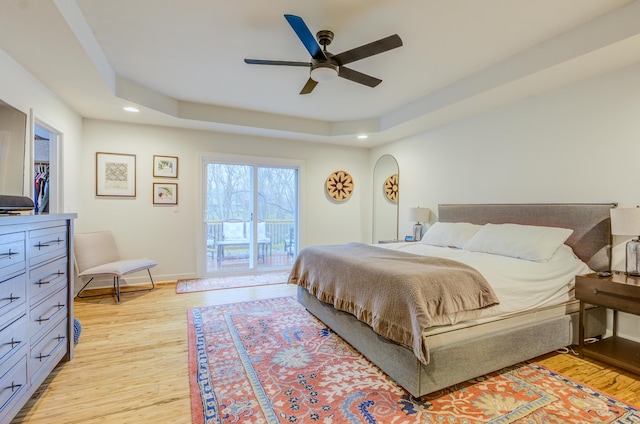bedroom featuring baseboards, light wood-style floors, a tray ceiling, recessed lighting, and access to exterior