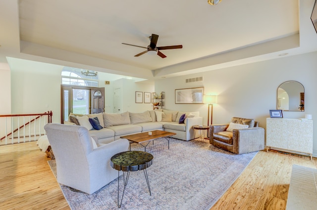 living area with a raised ceiling, visible vents, a ceiling fan, and wood finished floors