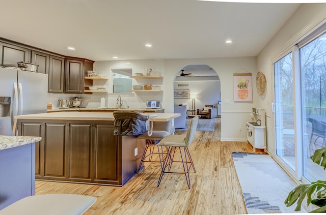 kitchen with fridge with ice dispenser, open shelves, a center island, recessed lighting, and light wood-style flooring