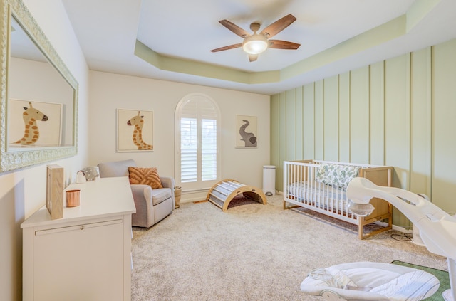 bedroom with a tray ceiling, carpet flooring, ceiling fan, and a nursery area
