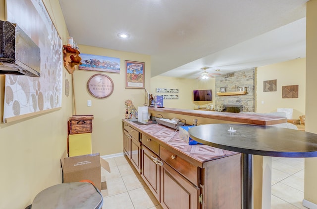kitchen with ceiling fan, a fireplace, a peninsula, light tile patterned flooring, and open floor plan